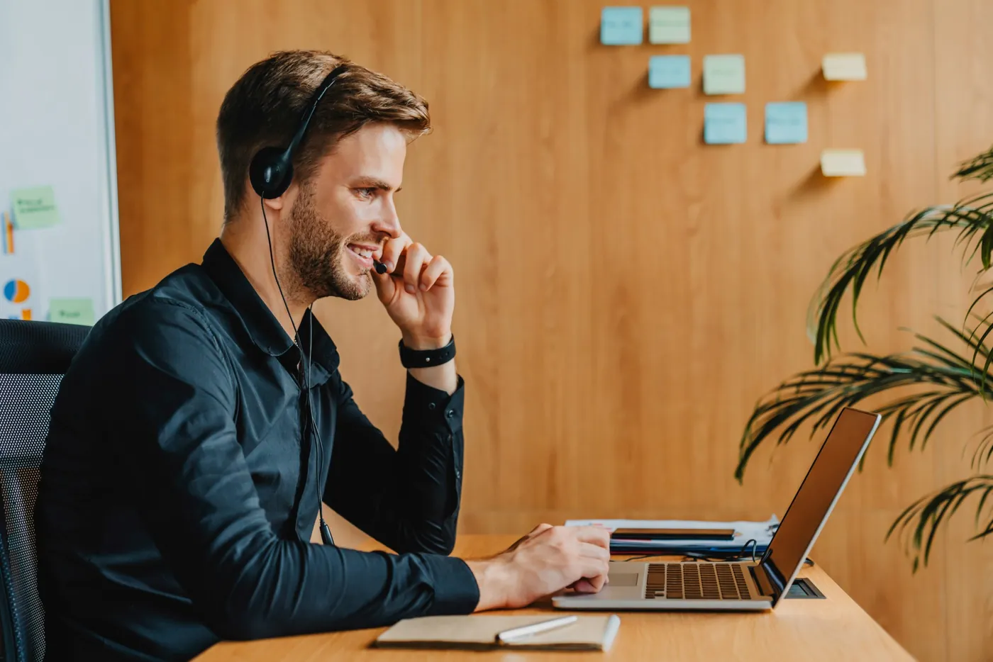 Mann mit Headset führt lächelnd ein Gespräch am Laptop